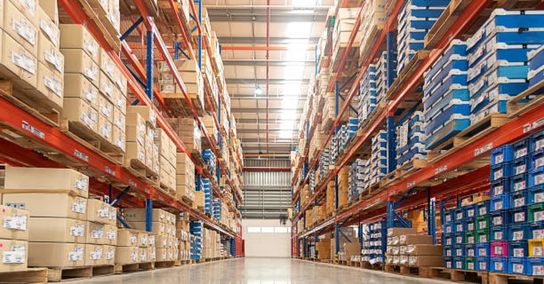 Rows of shelves with goods boxes in huge distribution warehouse at industrial storage factory.